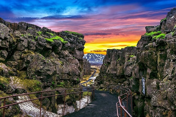 A railed path running down between mossy lava walls under a sunset sky