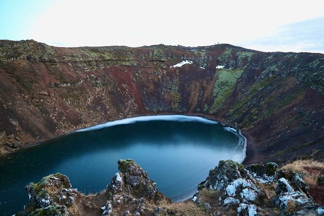 A crater lake with snow on the scoria rim and dark water below