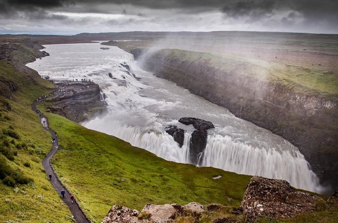 Gullfoss dropping into its canyon under a grey sky, a cliff path running beside it