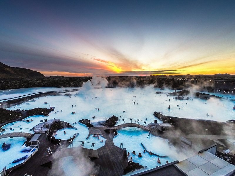 A milky-blue geothermal lagoon among black lava under an orange evening sky